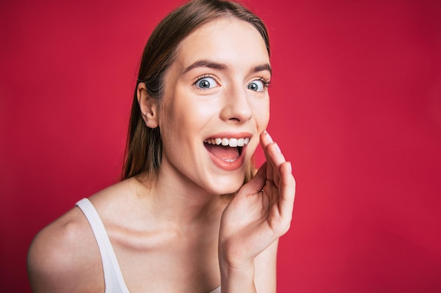 Joven mujer emocionada y feliz con cara de sorpresa mira a la cámara sobre la pared rosa