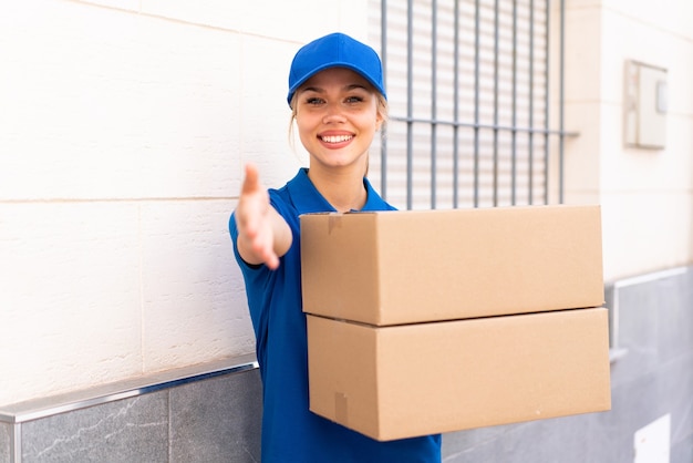 Joven mujer de entrega al aire libre sosteniendo cajas con expresión feliz haciendo un trato