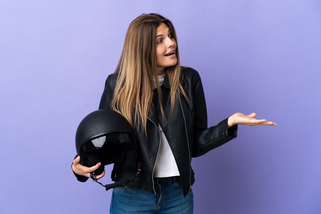 Joven mujer eslovaca sosteniendo un casco de motocicleta aislado en la pared púrpura con expresión de sorpresa mientras mira de lado