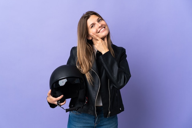 Joven mujer eslovaca sosteniendo un casco de motocicleta aislado en púrpura feliz y sonriente