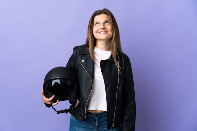 Joven mujer eslovaca sosteniendo un casco de motocicleta aislado sobre fondo púrpura pensando en una idea mientras mira hacia arriba