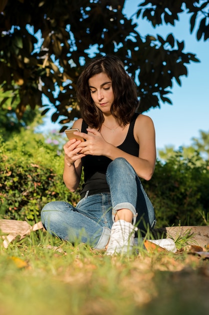 Joven mujer está usando su teléfono inteligente en un parque