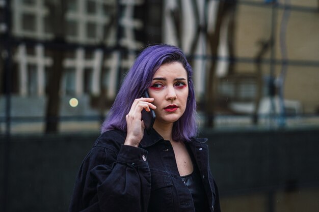 Foto joven mujer europea con cabello morado caminando por la calle y hablando por su teléfono