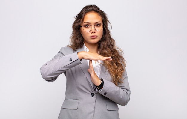 Joven mujer expresiva con gafas y elegante traje posando en la pared blanca