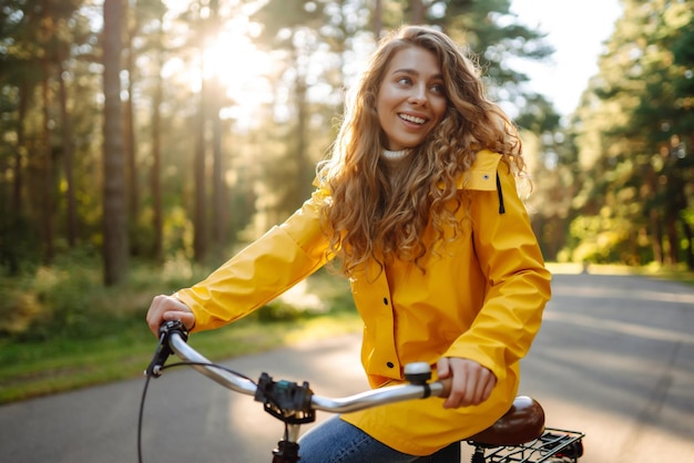 Joven mujer feliz con abrigo amarillo monta en bicicleta en un parque soleado Concepto de naturaleza relajante Estilo de vida