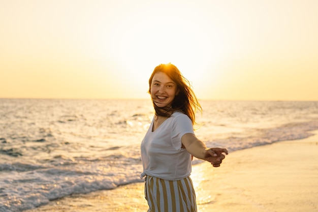 Joven mujer feliz bailando dando la vuelta por el mar con un vestido amarillo revoloteando Paisaje marino al amanecer con un hermoso cielo La niña mira el amanecer mágico