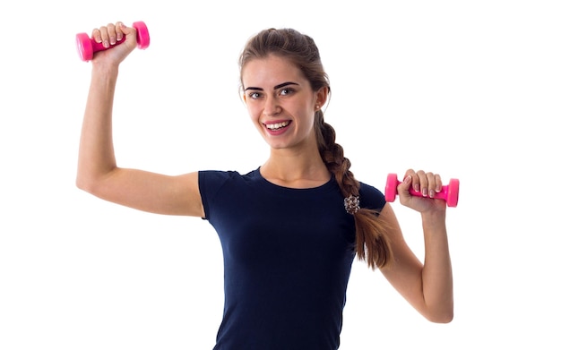 Joven mujer feliz con camiseta azul sosteniendo mancuernas rosas en sus manos sobre fondo blanco en el estudio