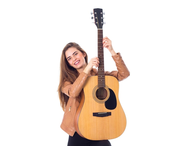 Joven mujer feliz con chaqueta marrón sosteniendo una guitarra con fondo blanco en el estudio