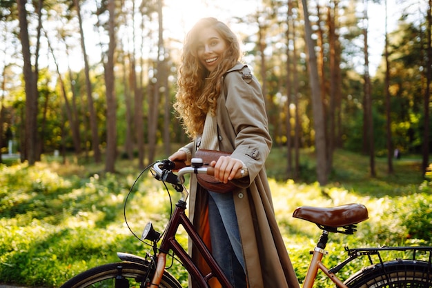 Joven mujer feliz monta bicicleta en el parque soleado Hermosa mujer disfruta de la naturaleza otoñal Estilo de vida