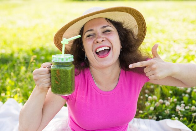 Joven mujer feliz muestra batidos verdes en un picnic. Concepto de dieta, desintoxicación y comida sana.