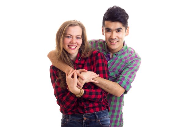 Joven mujer feliz con el pelo castaño largo y un hombre joven y guapo con el pelo oscuro en camisas a cuadros abrazándose sobre fondo blanco en el estudio