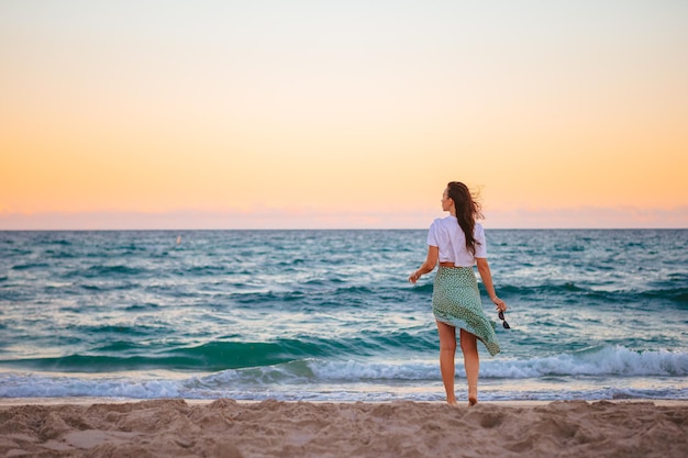 Joven mujer feliz en la playa al atardecer disfruta de su vista del cielo