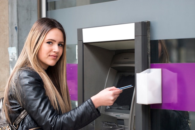 Joven mujer feliz retirando dinero de la tarjeta de crédito