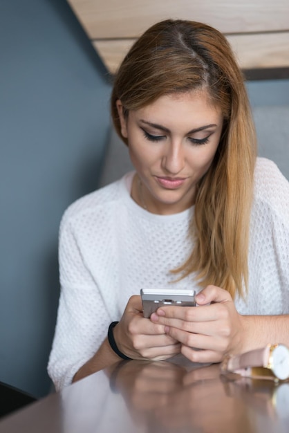 joven mujer feliz sentada en la mesa y usando el teléfono móvil en una casa de lujo