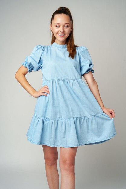 Foto joven mujer feliz y sonriente en un vestido azul claro sobre un fondo gris