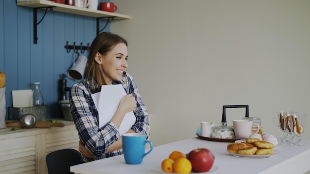 Joven mujer feliz sorprendida de recibir buenas noticias leyendo una carta en la cocina