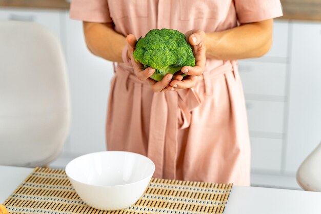 Joven mujer feliz sosteniendo brócoli en la hermosa cocina Concepto de dieta y comida saludable Perder peso