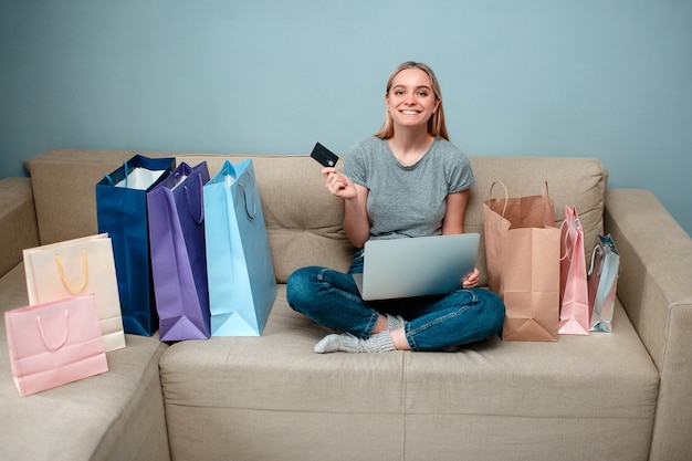 Foto joven mujer feliz con tarjeta de crédito sentado en el sofá con varias bolsas de compras