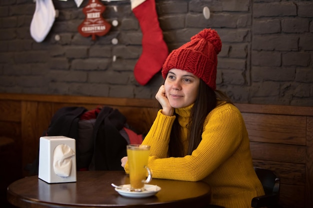Joven mujer feliz con traje de invierno de sombrero rojo sentada en un café bebiendo té caliente