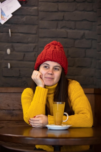 Joven mujer feliz con traje de invierno de sombrero rojo sentada en un café bebiendo té caliente