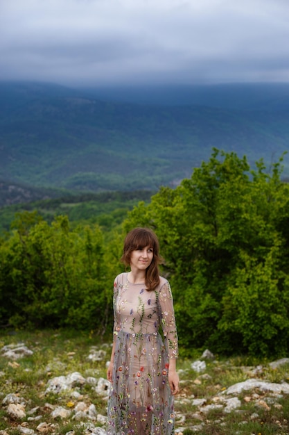 Joven mujer feliz con vestido largo en la ladera de la montaña Chica en la naturaleza sobre fondo de cielo azul Foto de moda