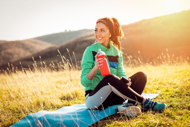 Joven mujer fitness descansando y refrescándose con agua, después de un duro entrenamiento en el prado.