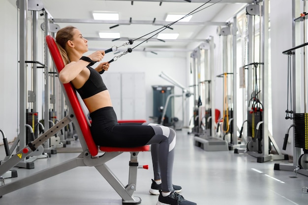 Joven mujer fitness entrenando en la máquina de ejercicio de cable de tracción en el gimnasio de la clínica de rehabilitación