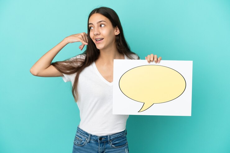 Foto joven mujer francesa aislada sobre fondo azul sosteniendo un cartel con el icono de la burbuja del discurso y haciendo gesto de teléfono