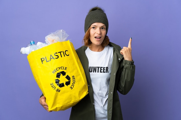 Joven mujer georgiana sosteniendo una bolsa llena de botellas de plástico para reciclar pensando en una idea apuntando con el dedo hacia arriba