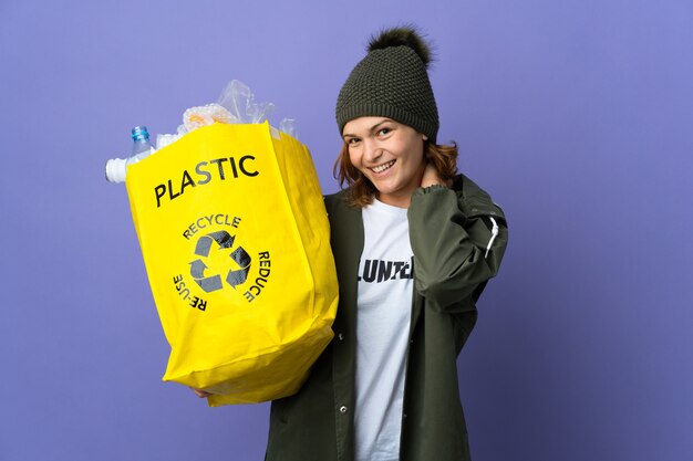 Joven mujer georgiana sosteniendo una bolsa llena de botellas de plástico para reciclar riendo