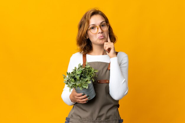 Joven mujer georgiana sosteniendo una planta aislada sobre fondo amarillo pensando en una idea