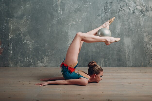 Joven mujer gimnasta profesional baila gimnasia rítmica con pelota en el estudio