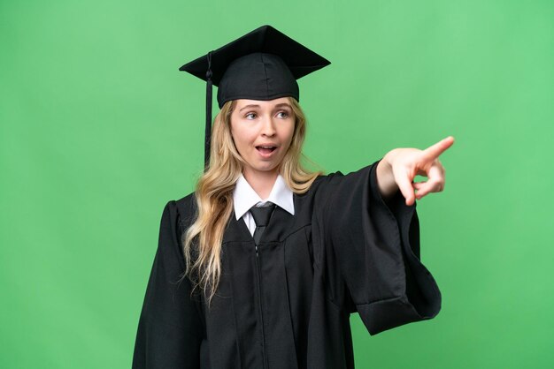 Joven mujer graduada en inglés universitario sobre un fondo aislado apuntando lejos