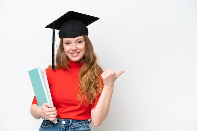 Joven mujer graduada universitaria aislada de fondo blanco apuntando hacia un lado para presentar un producto