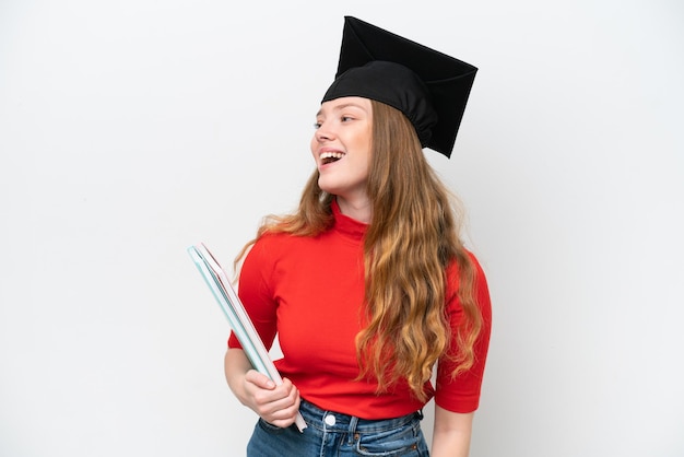 Joven mujer graduada universitaria aislada de fondo blanco riéndose en posición lateral