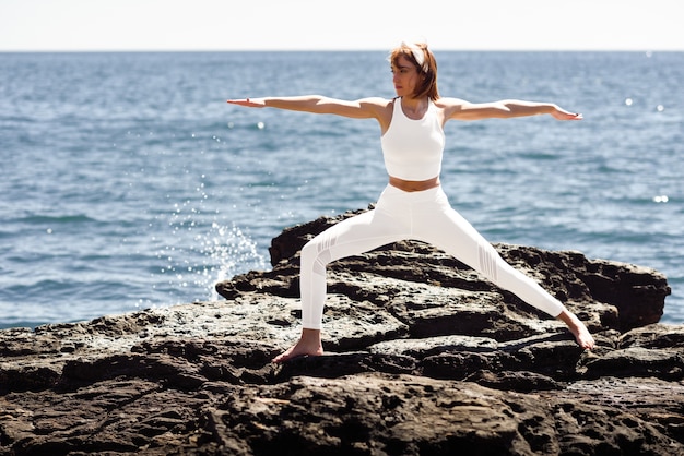 Joven mujer haciendo yoga en la playa con ropa blanca