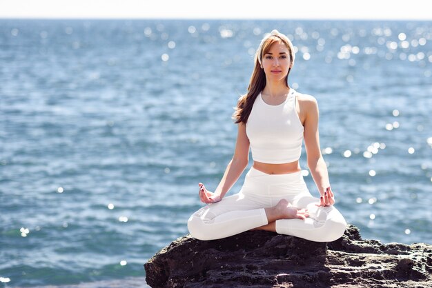 Joven mujer haciendo yoga en la playa con ropa blanca