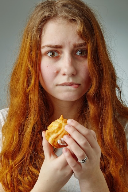 Joven mujer hermosa a dieta sentada frente a un delicioso pastel de crema, mirándolo apreciativamente, concepto de estilo de vida saludable, estudio, fondo gris