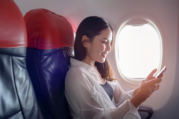 Joven mujer hermosa está usando un teléfono inteligente en el concepto de viajes y vacaciones en avión