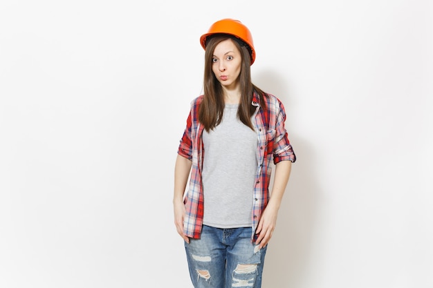 Joven mujer hermosa indiferente en ropa casual y casco naranja de construcción protectora aislado sobre fondo blanco. Instrumentos, accesorios para habitación de apartamento de renovación. Reparar el concepto de hogar.