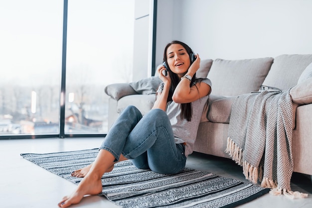 Joven mujer hermosa con ropa informal sentada sola en casa y escuchando música con auriculares.