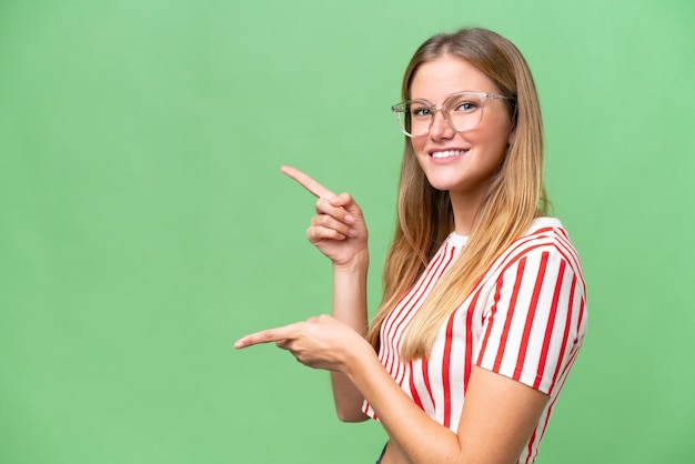 Joven mujer hermosa sobre un fondo aislado señalando con el dedo hacia un lado y presentando un producto