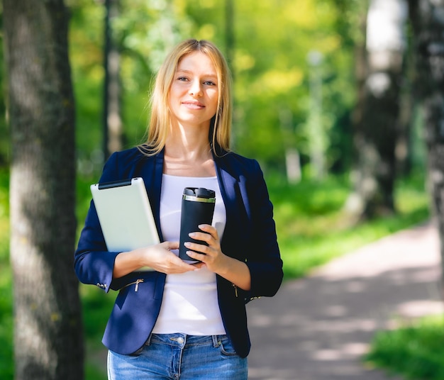 Joven mujer hermosa sonriente en el parque con un dispositivo de tableta y auriculares inalámbricos disfrutando del trabajo remoto del concepto de energía verde