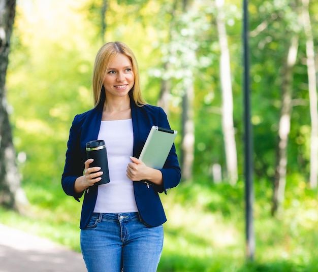 Joven mujer hermosa sonriente en el parque con un dispositivo de tableta y auriculares inalámbricos disfrutando del trabajo remoto del concepto de energía verde