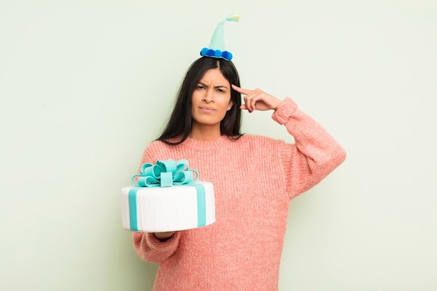 Joven mujer hispana bonita que se siente confundida y perpleja mostrando que eres un concepto loco de pastel de cumpleaños