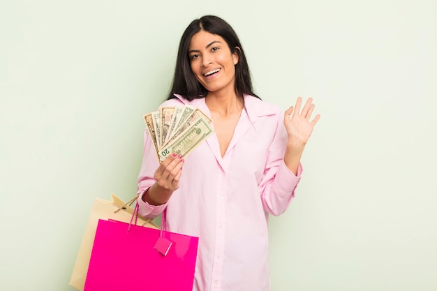 joven mujer hispana bonita sonriendo alegremente, saludando con la mano, dándote la bienvenida y saludándote. concepto de bolsas de compras