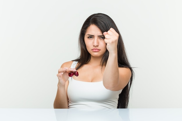 Joven mujer hispana con cerezas mostrando puño, agresiva expresión facial.