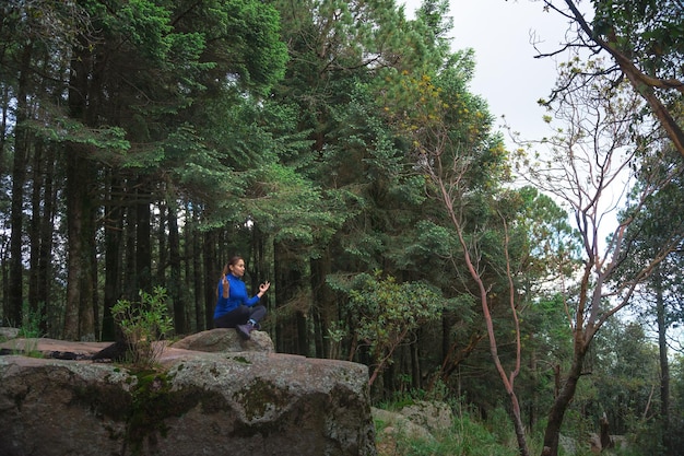 Una joven mujer hispana practicando yoga en un acantilado en un bosque