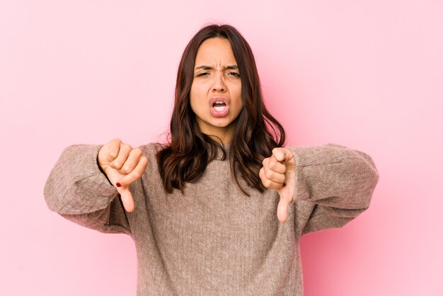 Joven mujer hispana de raza mixta aislada mostrando el pulgar hacia abajo y expresando aversión.