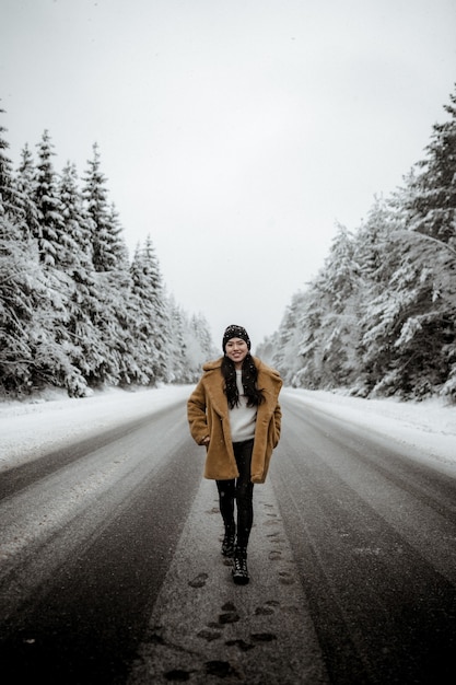 Joven mujer hispana sonriente en un elegante abrigo posando en el pintoresco bosque de invierno